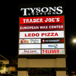 Illuminated Tysons Station tenant pylon sign displaying multiple business names at night.